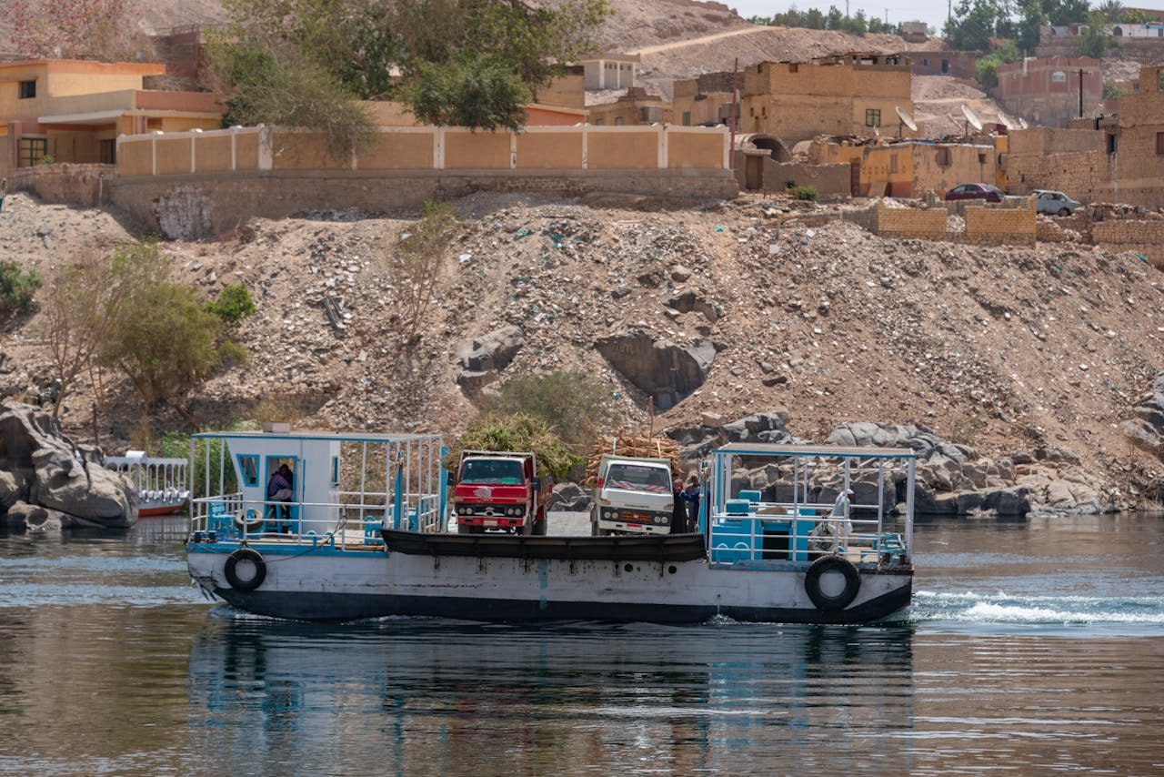 A barge transporting vehicles across a river with a rustic town in the background.